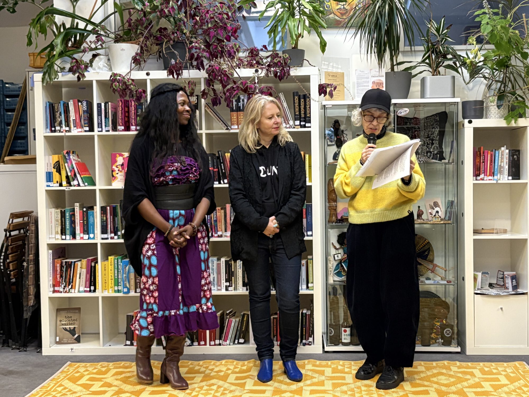 Drei Personen bei der Eröffnung der Ausstellung FASIA, vor einer Bücherwand. Von links nach rechts: Millicent Adjei, Joanna Warsza, Ina Wudtke